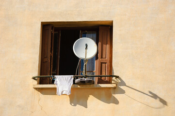 Satellite dish and drying singlet on window railing. Boredom concept. 