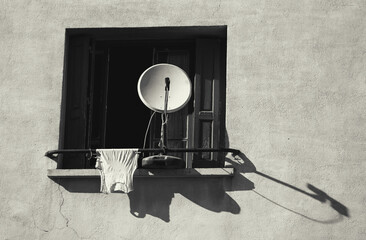 Satellite dish and drying singlet on window railing. Boredom concept. Black white historic photo.