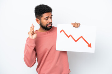 Young Brazilian man isolated on white background holding a sign with a decreasing statistics arrow symbol with fingers crossing
