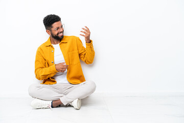 Young Brazilian man sitting on the floor isolated on white background making guitar gesture