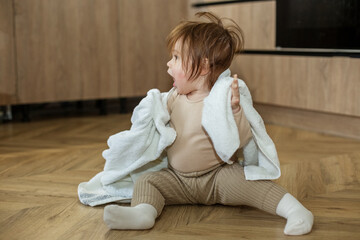 Portrait of a cute little girl sitting on the floor and playing with her blanket.