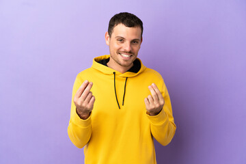 Brazilian man over isolated purple background making money gesture