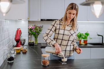 Woman pouring almond milk into a glass in kitchen. Healthy vegan product concept.