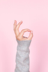 Female hand in gray knitted sweater with beautiful natural manicure - pink nude nails making ok...