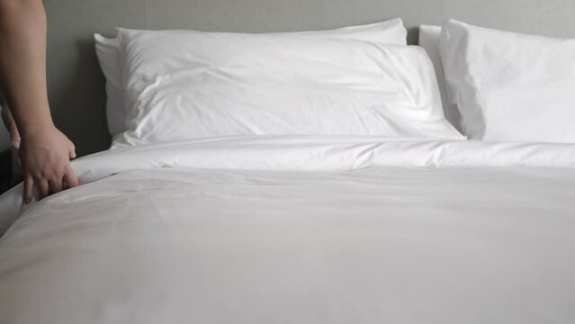 hotel service concept, housekeeper man arrange the pillow on the bed with white sheet, make bed in morning