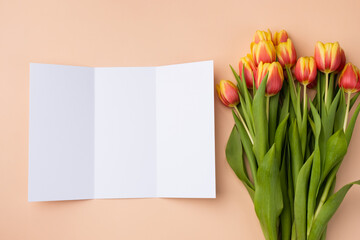 Mockup of trifold brochure on a beige background with a bouquet of tulips.