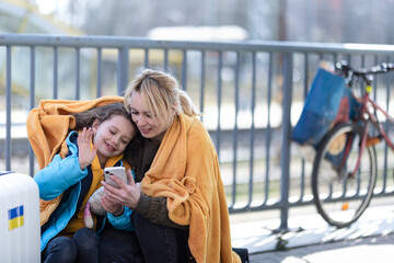 Ukrainian immigrants mother with daughter with luggage waiting at train station, Ukrainian war...