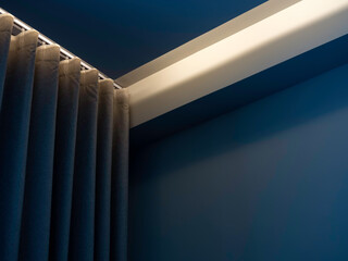 Close-up of blue wall curtain on curtain rail decorated with hidden light under the ceiling near...