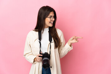 Fototapeta premium Young photographer Brazilian girl isolated on pink background pointing finger to the side and presenting a product