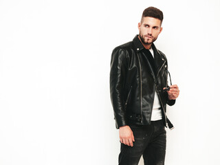 Portrait of handsome confident model. Sexy stylish man dressed in biker leather jacket and black jeans. Fashion hipster male isolated on white in studio. Holding sunglasses