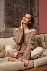 Obraz premium a beautiful woman with dark hair in cozy clothes is sitting on the sofa, hugging her neck. naturalness, naturalness
