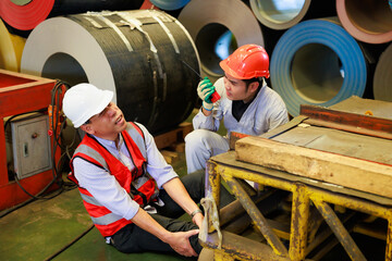 First Aid. Engineering supervisor talking on walkie talkie communication while his coworker lying unconscious at industrial factory. Professional engineering teamwork concept.