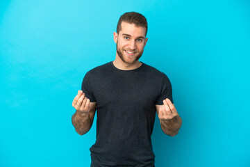 Young handsome caucasian man isolated on blue background making money gesture