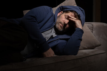 Senior Mann mit Migräne oder Depressionen hat sich einsam im dunkeln auf seine Couch zurück...