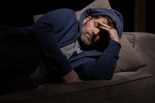 Senior Mann mit Migräne oder Depressionen hat sich einsam im dunkeln auf seine Couch zurück gezogen.