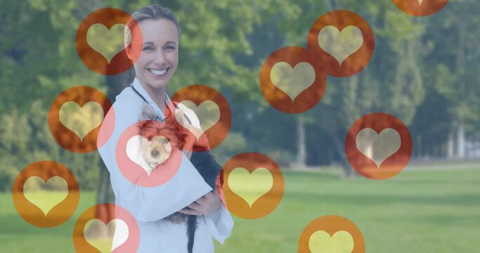 Animation of heart icons moving over smiling female vet holding dog