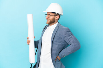 Young architect man with helmet and holding blueprints over isolated background suffering from backache for having made an effort