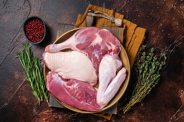 Fresh duck meat parts, raw breast steak, legs, wings in a plate with herbs. Dark background. Top...