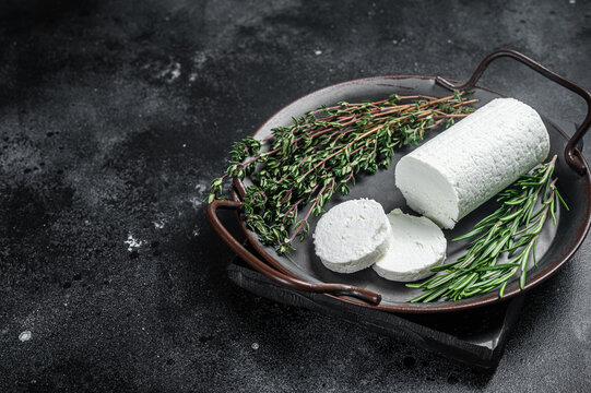 Chevre goat soft cheese with herbs on a tray. Black background. Top view. Copy space