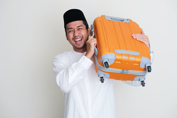 Moslem Asian man smiling happy while carrying travelling suitcase