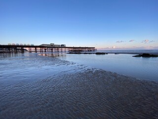 Hastings, East Sussex, UK - Hastings pier with beach huts at low tide reflections on the sand 