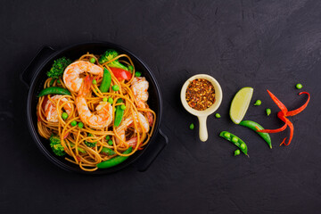 Stir-fried spaghetti or stir-fry noodles with vegetables and shrimp in a black bowl. dark...