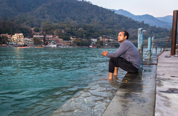 isolated young man sitting at ganges river bank from flat angle