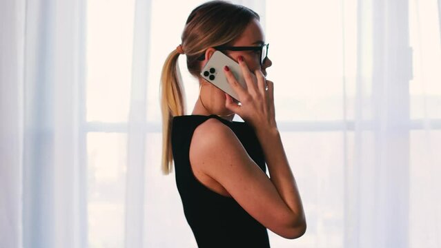 4k Elegant businesswoman in glasses and black dress. Office concept. Brown and modern interior. Talking and working on laptop.
