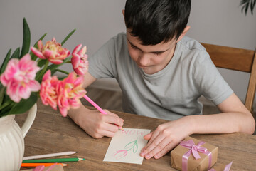 The boy makes a card for mother's day. Materials for artistic creativity on the children's table, children's drawings.