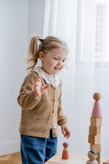 happy girl looking at tower made of wooden cubes and figurine while playing at home.