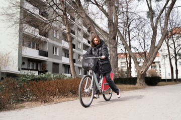 Young beautiful woman taking a bicycle by bike-sharing service and using application by phone outside on the street. Female student renting a bike