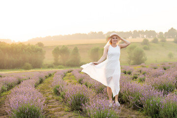 Fototapeta na wymiar Beautiful young woman walking the field of lavender. Fashion outfit dress, straw hat.