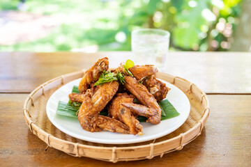 Salted chicken wings on a white plate placed in a woven bamboo basket.