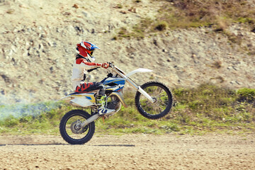 Naklejka na ściany i meble Motocross driver in action accelerating the motorbike takes off and jumps on springboard on the race track.