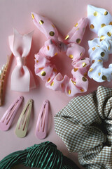 Colorful scrunchies, emerald green headband and pearl hair clips on pastel pink background. Flat lay.