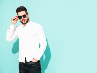 Portrait of handsome confident  model. Sexy stylish man dressed in white shirt and jeans. Fashion hipster male posing near blue wall in studio. Isolated. In sunglasses