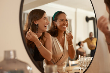 We always have a joke prepared. Shot of two young friends standing together and using a mirror to touch up their makeup at a dinner party. - obrazy, fototapety, plakaty