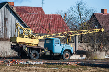 An old, rusty soviet truck crane stands by the house.