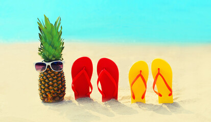 Summer vacation concept - pineapple with sunglasses and colorful flip flops on beach over sea...