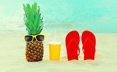 Summer vacation concept - pineapple with sunglasses, cup of juice and colorful flip flops on beach...