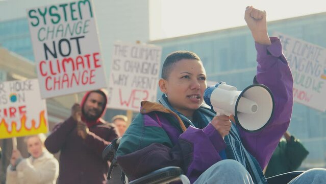 Female protestor in wheelchair using megaphone holding placards and chanting slogans on demonstration march to promote awareness of climate change - shot in slow motion