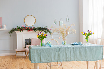 Spacious bright room with a table decorated with Easter eggs and bouquets of flowers and a blue tablecloth in daylight. - 498287905