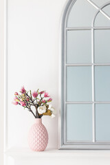 Pink magnolia flowers in a vase on a shelf near a mirror. The concept of minimalism in the interior.