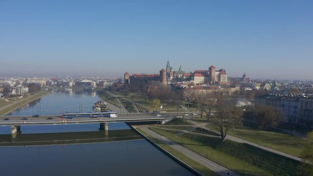 Drone camera moves from bottom to top, panoramic view of castle on Wawel hill and urban city in morning fog. Beautiful aerial video footage Krakow Poland. Tram at Grunwaldzki bridge River Visla  