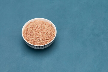 Pink oriental Devzira rice for pilaf in bowl. Selective focus, blue background, copy space