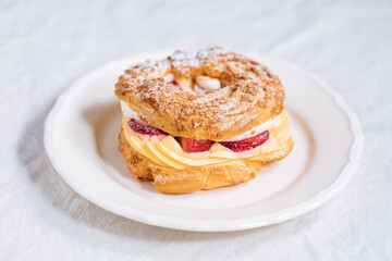 Traditional French Dessert called Paris Brest on a light grey background with powder sugar and strawberries