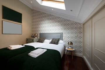 Bedroom with double bed with green cushions and blankets, skylight in the ceiling, wall with decorative paper and fitted wardrobes with sliding wooden doors