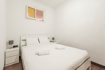 Bedroom with king size bed with white wooden headboard with matching side tables and rolled up white towels