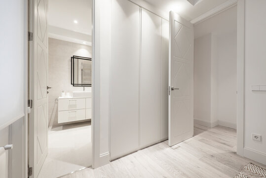 Bedroom with en-suite bathroom and dressing room with cabinets with white wooden doors and light wooden floors