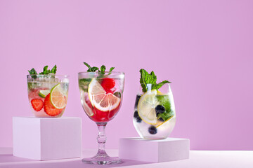 Summer refreshing fruit and berry infused detox water on podiums in pink color, creative summer beverages background